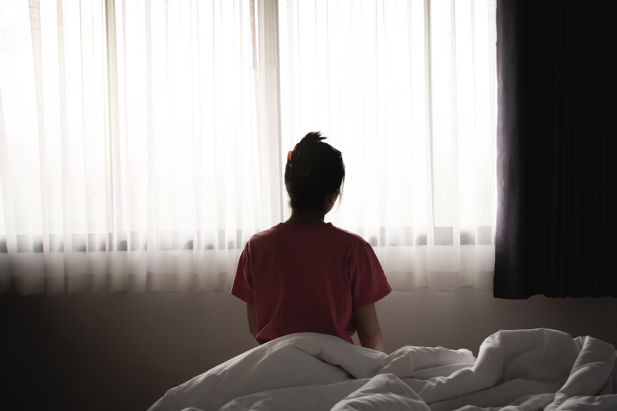 Image of woman sat on bed looking at out a window.