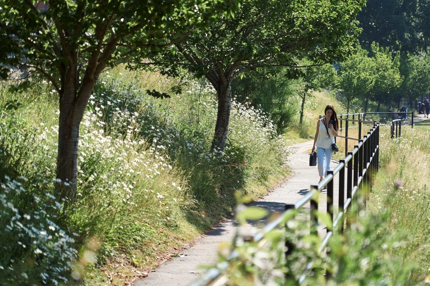 A woman walks along a path, surrounded by greenery and trees.