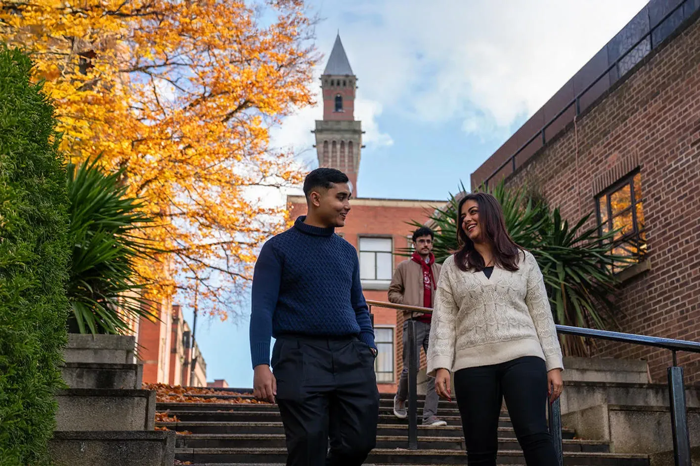 Three students walking down some steps with Old Joe in the background